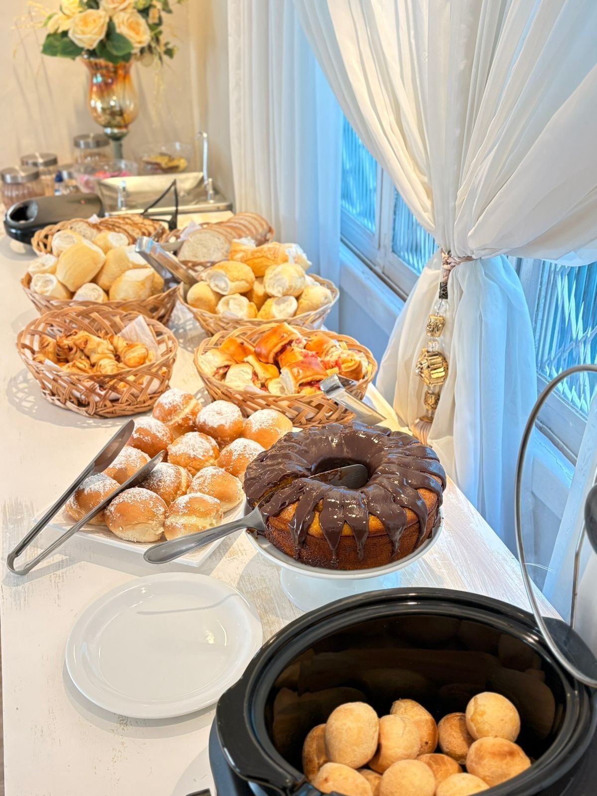 A buffet table with various baked goods, including bread, pastries, and a chocolate bundt cake.
