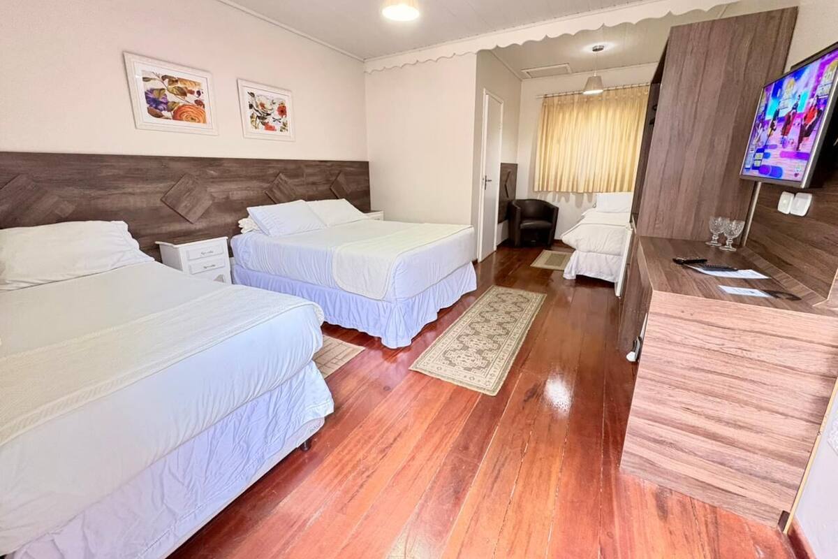 A hotel room with two beds, a wooden floor, a desk with a TV, and framed pictures on the wall.