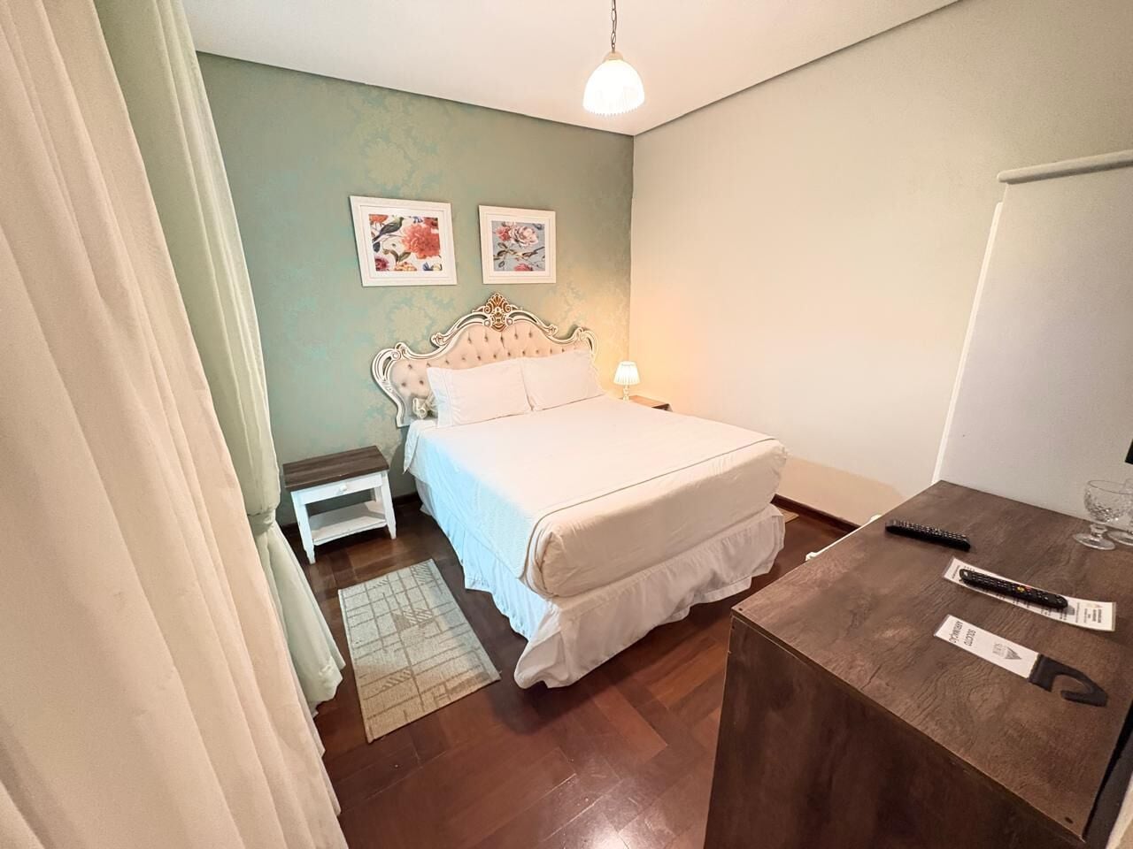 A bedroom with a bed, bedside table, lamp, and two framed pictures on the wall.