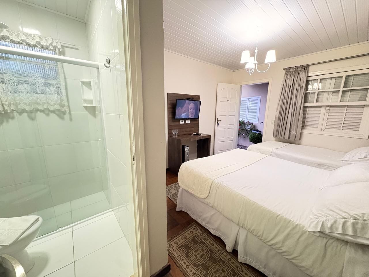 Hotelkamer met douche, bed, televisie en bureau met stoel.