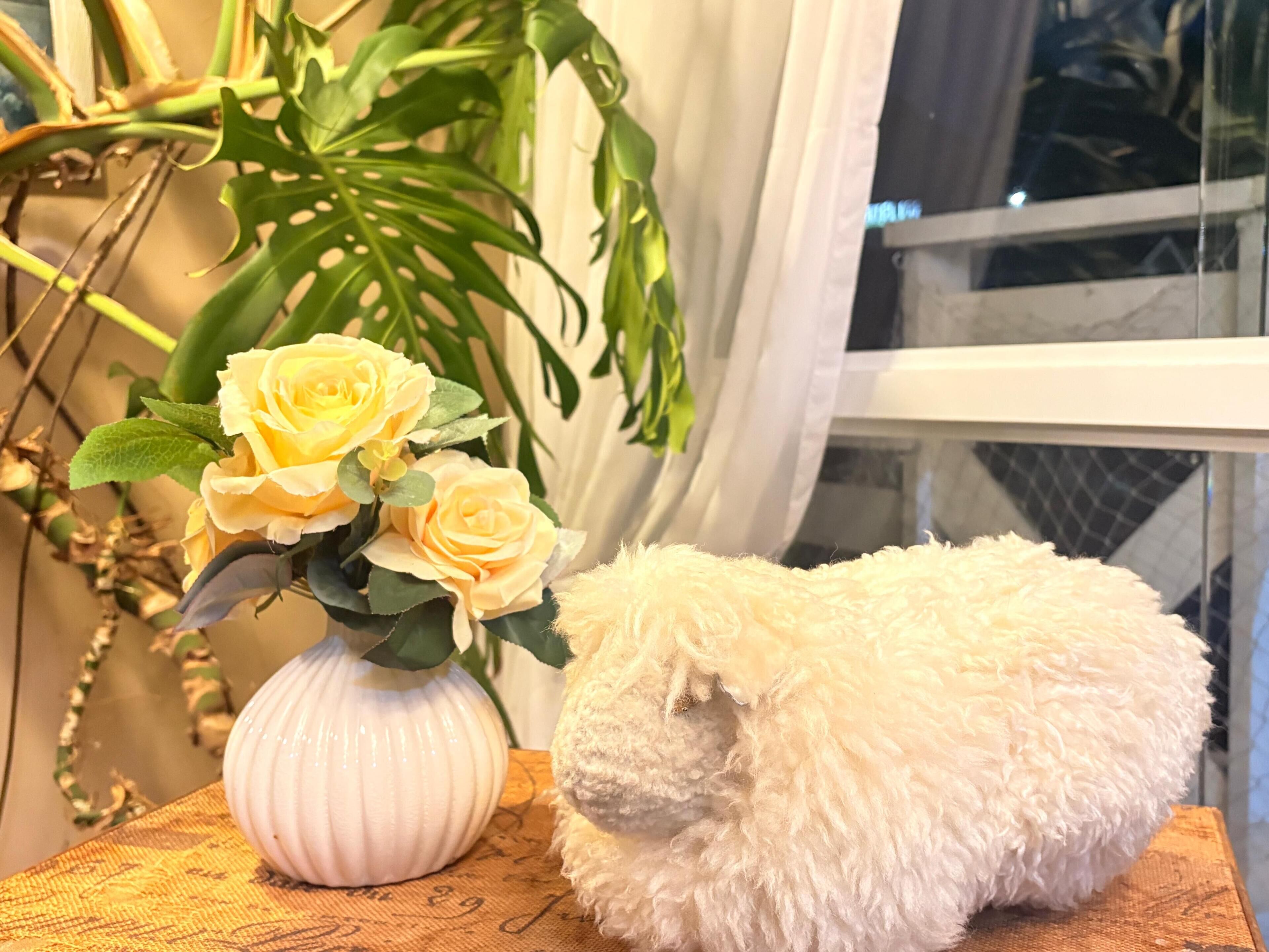 A white fluffy object on a wooden surface next to a white vase with yellow roses.