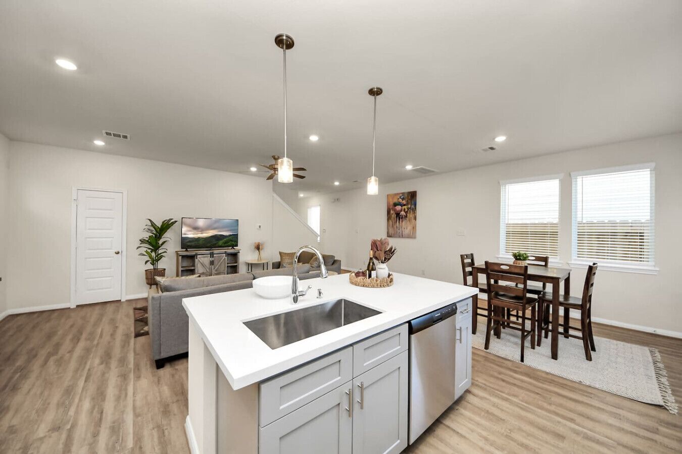 A modern kitchen with a central island, a dining area with wooden chairs, and a living room with a sofa and TV.