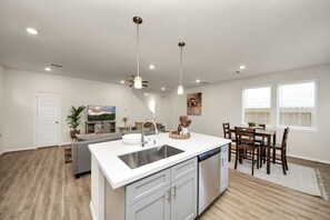 Eine moderne Küche mit Kochinsel, ein Essbereich mit Holzkästen und ein Wohnzimmer mit Sofa und Fernseher.