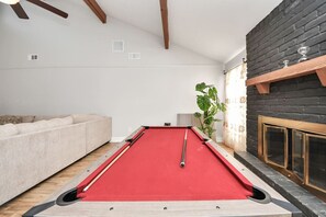 A pool table in a room with a sofa, a plant, and a fireplace.