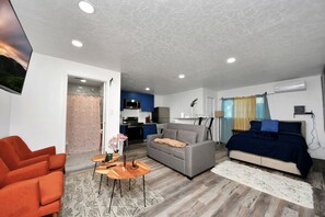 A modern living room with a sofa, a dining table, and a kitchen in the background.