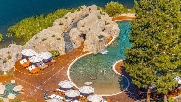 Vue aérienne d’un complexe hôtelier comprenant une formation rocheuse, une piscine et des espaces de détente avec des parasols.