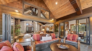 Un vaste espace de vie doté d’un plafond en bois, de grandes fenêtres et d’un coin salon confortable.