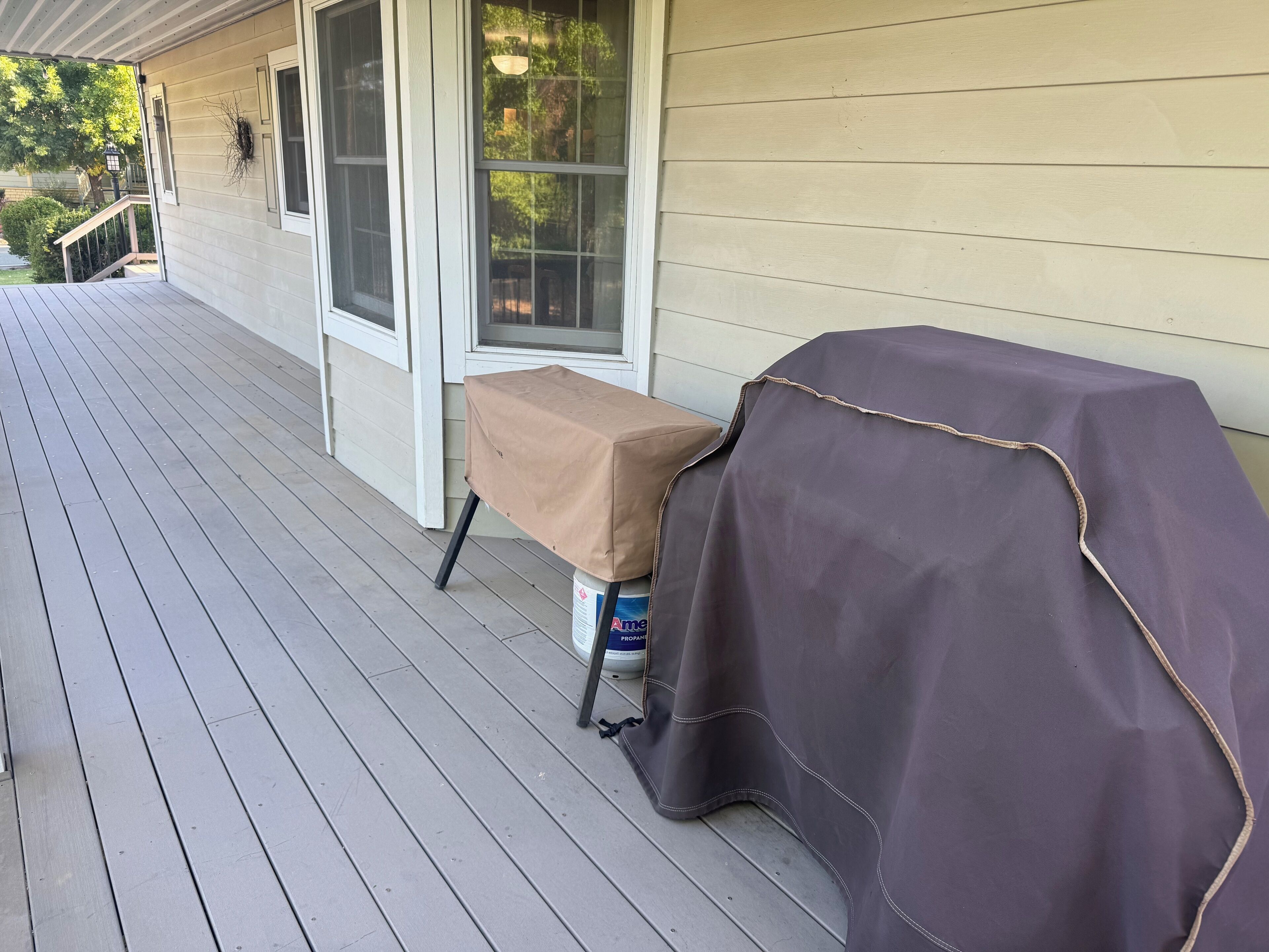A covered outdoor table with a grill on a wooden deck.