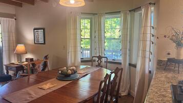 Un comedor con mesa de madera, sillas, lámpara y ventana con cortinas.