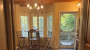 Une pièce au plancher de bois, avec une table à manger et des chaises, un lustre et une vue par la fenêtre.