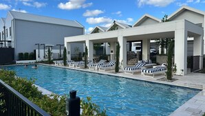A swimming pool with lounge chairs and a covered area, surrounded by modern buildings.