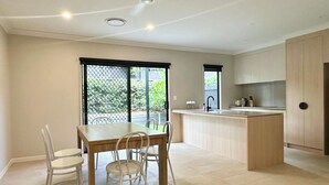 A modern kitchen with a dining area, featuring a central island, a built-in oven, and a large window with a view of greenery.