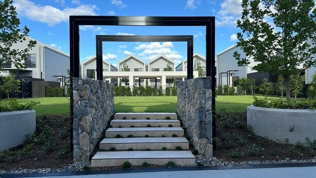 A modern building with a symmetrical facade, a central staircase leading to a gated entrance, and a well-maintained lawn.