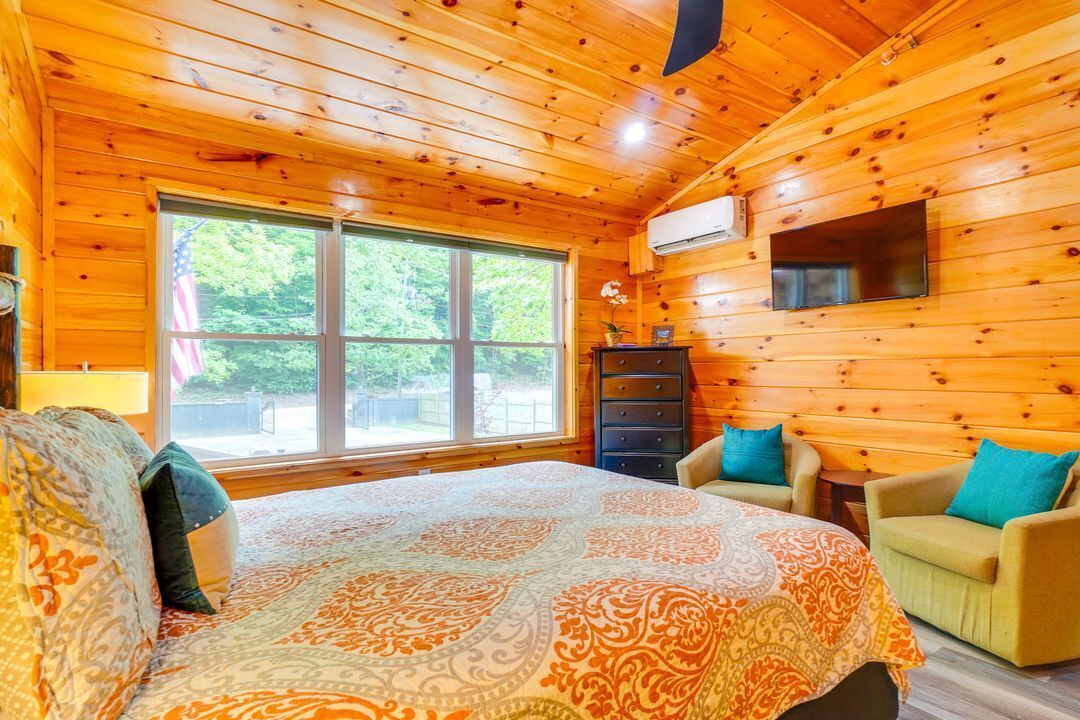 Habitación de cabaña de madera con una cama grande, un tocador, un televisor y una ventana con vista a árboles.