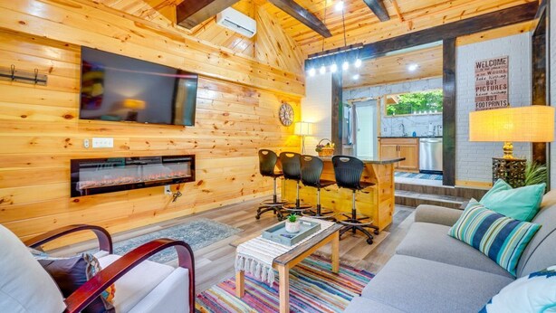 A cozy wooden cabin interior with a living room, a fireplace, a TV, and a kitchen area. - Absolute Humble Abode, Condo, Sleeps 4, Mins from Dollywood! (Pigeon Forge)