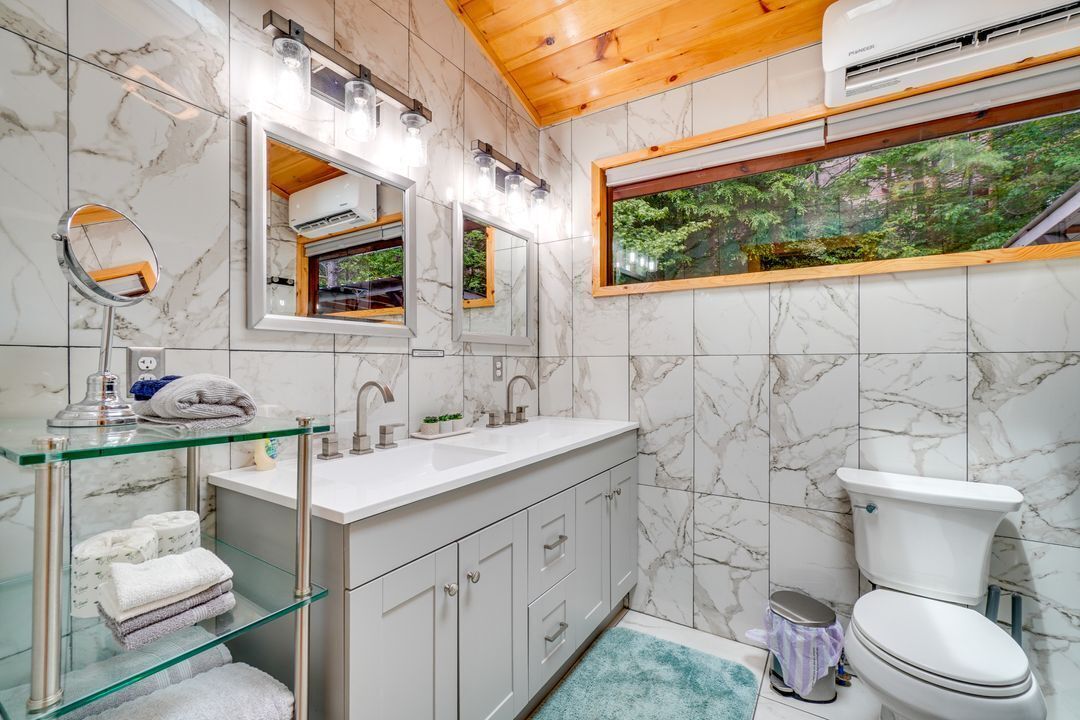 Een moderne badkamer met marmeren wanden, een glazen wastafel, toilet en raam met uitzicht op een bos.