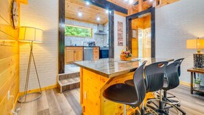 A modern kitchen with wooden accents, a central island with chairs, and a visible clock. - Absolute Humble Abode, Condo, Sleeps 4, Mins from Dollywood! (Pigeon Forge)