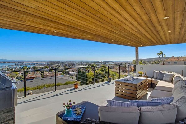 Eine Dachterrasse mit Holzboden, Sitzgelegenheiten im Freien, Blick auf die Stadt und ein Gewässer in der Ferne.
