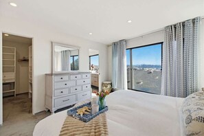 Ein Schlafzimmer mit einem großen Bett, einem Schminktisch, einem Spiegel und Blick auf das Wasser.