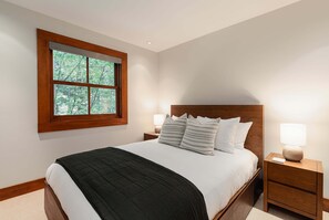 Ein Schlafzimmer mit einem großen Bett, einem Fenster mit Blick auf Bäume, zwei Nachttischen mit Lampen und einem Holzkopfende.