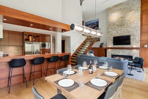 Eine moderne Küche mit Bar, ein Esszimmer mit Kamin und ein Wohnbereich mit Sofa und Fernseher.
