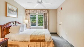 A hotel room with a bed, a nightstand, a ceiling fan, a window with curtains, and a door. - Cozy Condo in Beautiful Lake Harmony, Pocono Mountains (Lake Harmony)