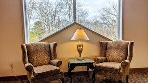 Two armchairs facing each other with a table and lamp between them, a large window with a view of trees, and patterned carpet. - Cozy Condo in Beautiful Lake Harmony, Pocono Mountains (Lake Harmony)