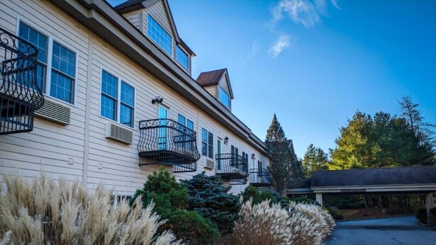 A two-story building with multiple balconies, a covered driveway, and landscaped areas with tall grasses and shrubs. - Cozy Condo in Beautiful Lake Harmony, Pocono Mountains (Lake Harmony)