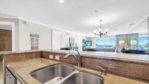 A modern kitchen with granite countertops, stainless steel sinks, and a view of the ocean through large windows. - Gulf Front-Amazing Views! Close to Dining & Shopping Crystal Dunes 404 (Destin)