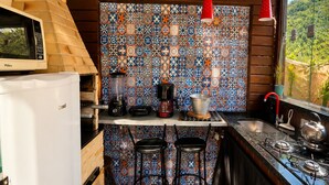 A compact kitchen with a wooden ceiling, a patterned backsplash, a built-in refrigerator, a coffee maker, and a gas stove.