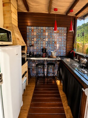A compact kitchen with a wooden ceiling, a patterned backsplash, a built-in refrigerator, a coffee maker, and a gas stove.
