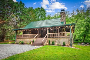 A lodge with a stone chimney, wooden porch, and a gravel driveway. - Toccozy Cabin Retreat - Riverfront | Pet Friendly | Hot Tub | Game Room | Firepit (Mineral Bluff)