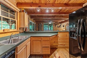 A wooden cabin kitchen with a large island, stainless steel sinks, and a black refrigerator. - Toccozy Cabin Retreat - Riverfront | Pet Friendly | Hot Tub | Game Room | Firepit (Mineral Bluff)