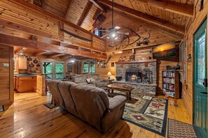 A log cabin interior with a fireplace, wooden furniture, and a stone wall. - Toccozy Cabin Retreat - Riverfront | Pet Friendly | Hot Tub | Game Room | Firepit (Mineral Bluff)