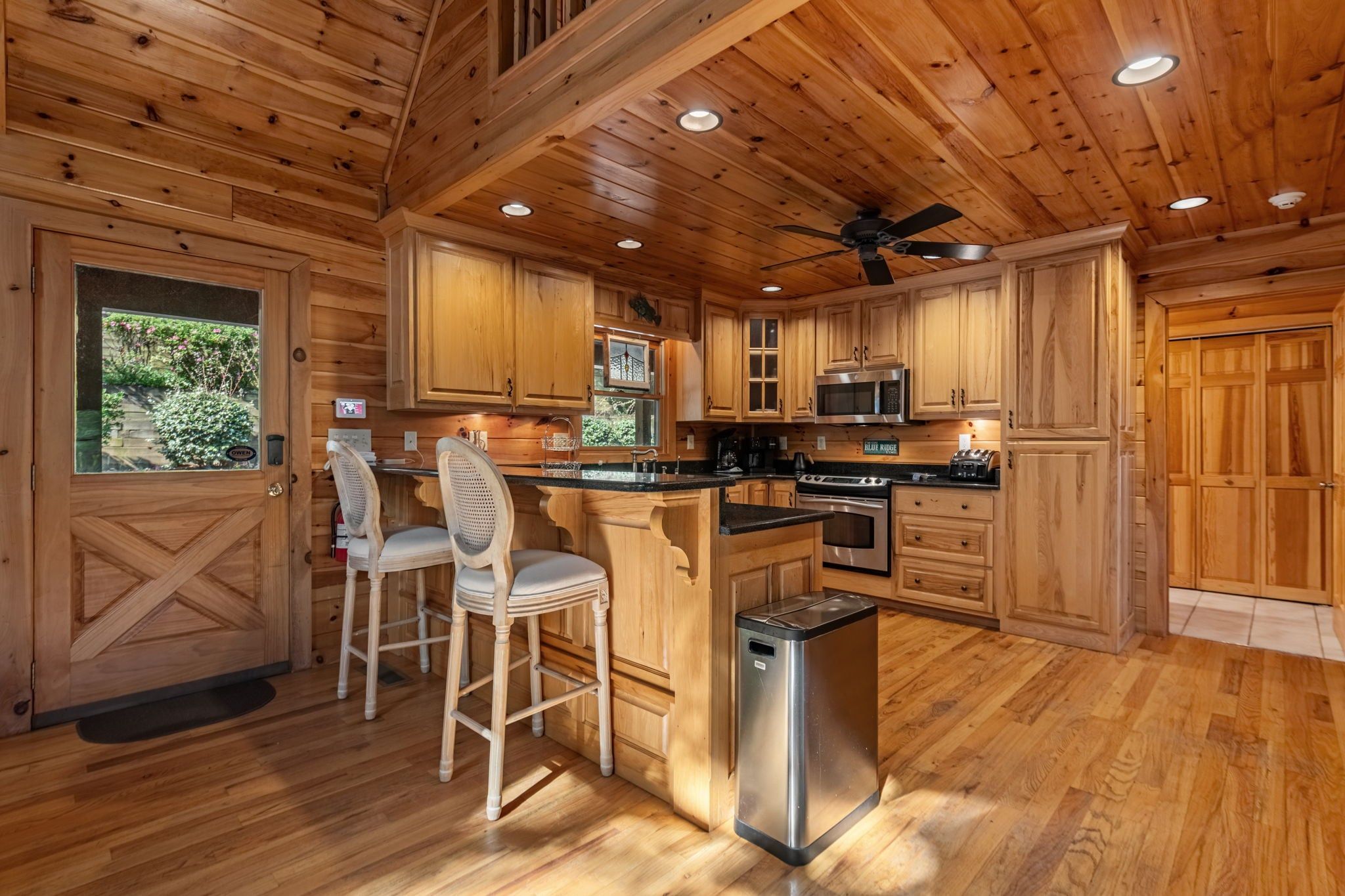 A wooden cabin interior with a kitchen, bar area, and a door leading outside.