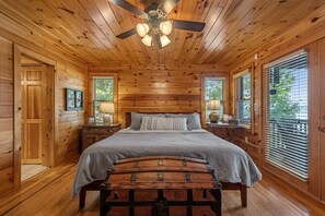 A wooden cabin bedroom with a bed, a bench, a ceiling fan, and a window with blinds. - Johnny's Lakeside Hideaway - Private Dock | Hot Tub | Game Room (Morganton)