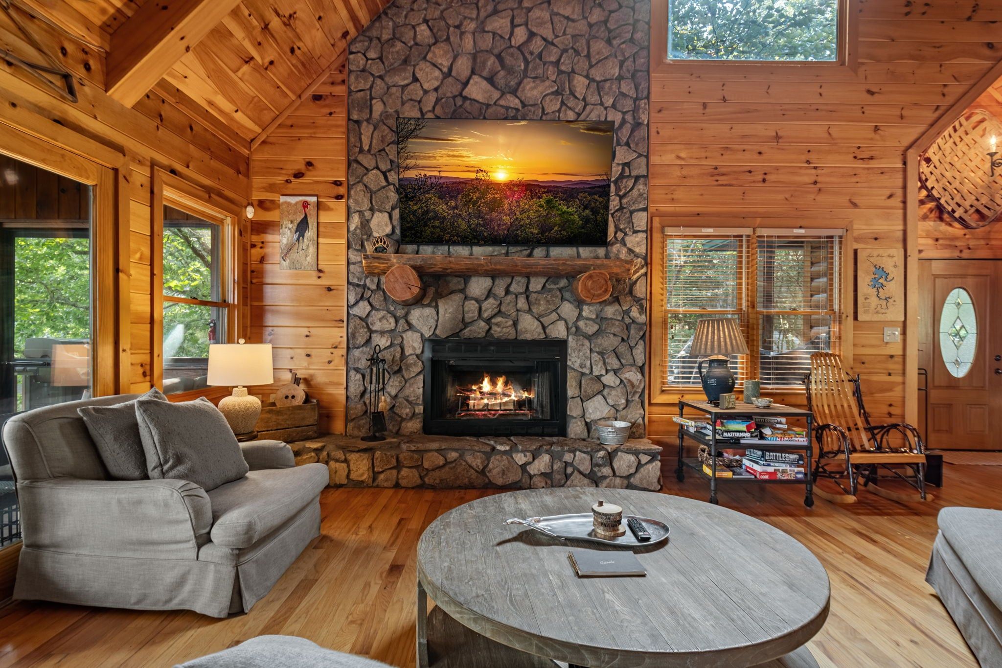 Un acogedor interior de cabaña con chimenea de piedra, muebles de madera y un amplio ventanal.