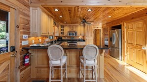 Eine Holzblockküche mit Kochinsel, zwei Barhocker, Deckenventilator und einem Edelstahlkühlschrank.