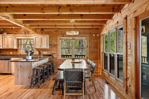 A wooden cabin interior with a kitchen, dining area, and large windows. - It's All About the Views - Mtn Views | Hot Tub | Pool Table | Arcade Games | Fire Pit (Blue Ridge)