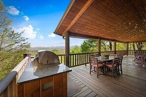 A wooden deck with a grill, dining table, and chairs, overlooking a mountainous landscape. - It's All About the Views - Mtn Views | Hot Tub | Pool Table | Arcade Games | Fire Pit (Blue Ridge)