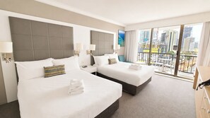 Ein Hotelzimmer mit zwei Betten, einem Balkon mit Blick auf die Stadt und einem Schreibtisch.