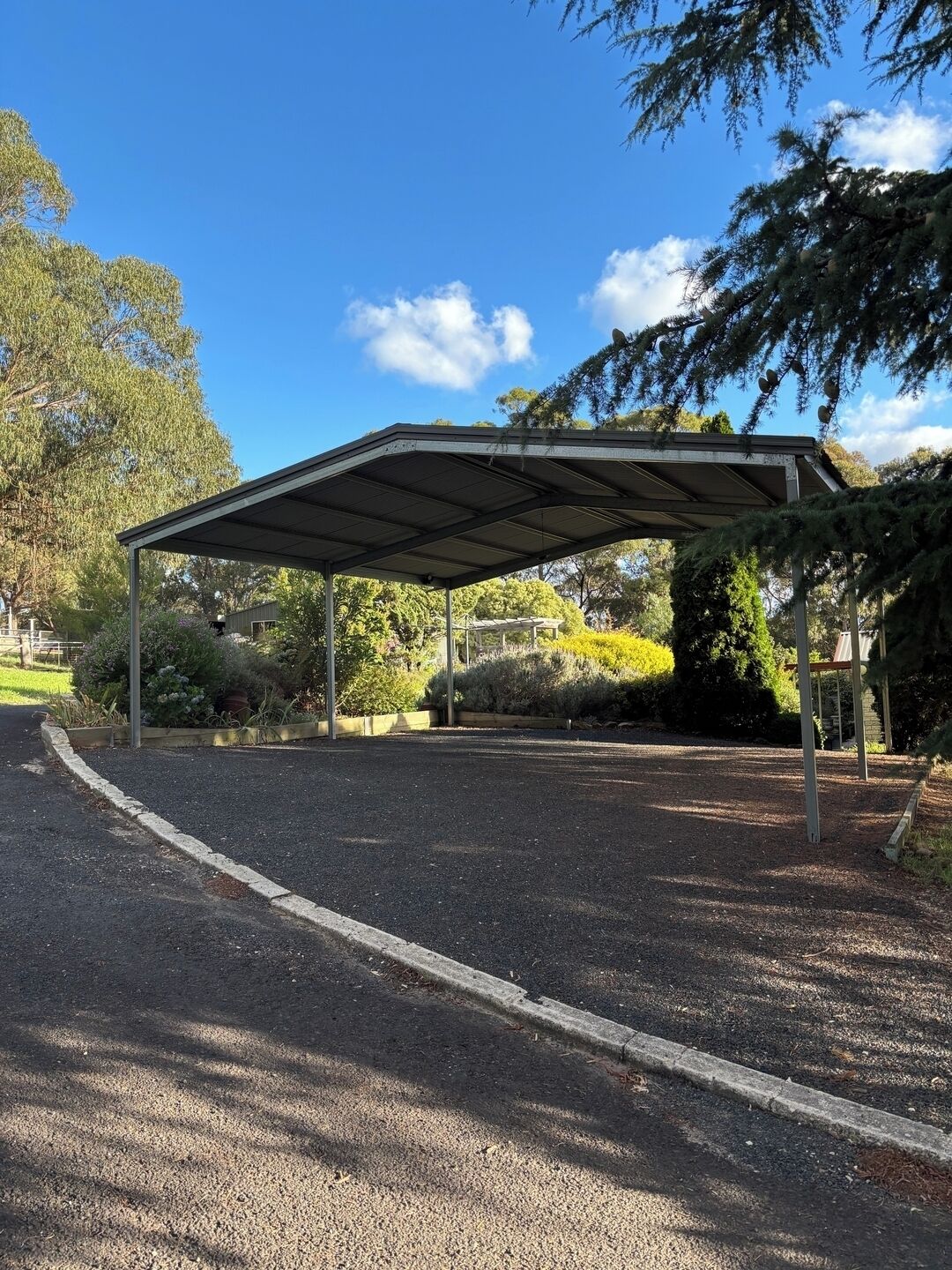 Un espace extérieur abrité, doté d’un chemin de gravier et entouré d’arbres et d’arbustes.