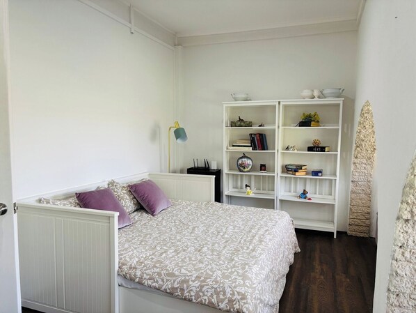A bedroom with a bed, a white radiator, a white bookshelf, and a stone accent wall.