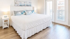 Ein Schlafzimmer mit einem großen Bett, einem Nachttisch, einem Gemälde und einer Balkontür.