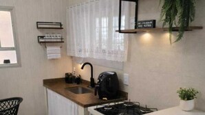 A compact kitchen with a white countertop, black chairs, a gas stove, and a potted plant. - Practical and cozy house in Vila Velha (2 guests) (Vila Velha)