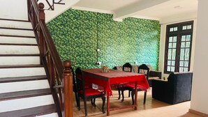 Ein Essbereich mit einer Holztreppe, einer grünen Wand aus Blättern, einem Tisch mit roter Tischdecke und einem schwarzen Sofa.