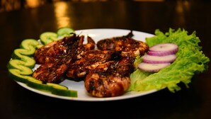 Ein Teller gegrilltes Fleisch mit Gurkenscheiben und roten Zwiebelringen auf einem Salatbett.