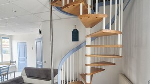 Ein modernes Interieur mit einer Wendeltreppe, einem grauen Sofa und einem Essbereich mit Tisch und Stühlen.