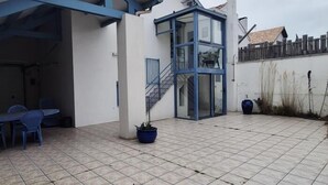 Ein überdachter Patio-Bereich mit Fliesenboden, einer Treppe zu einer erhöhten Ebene und einer Sitzgelegenheit mit Stühlen.