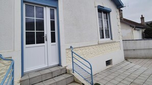 Ein Gebäude mit weißer Fassade und blauen Akzenten, inklusive einer Haustür, einem kleinen Fenster und einer Treppe zum Eingang.